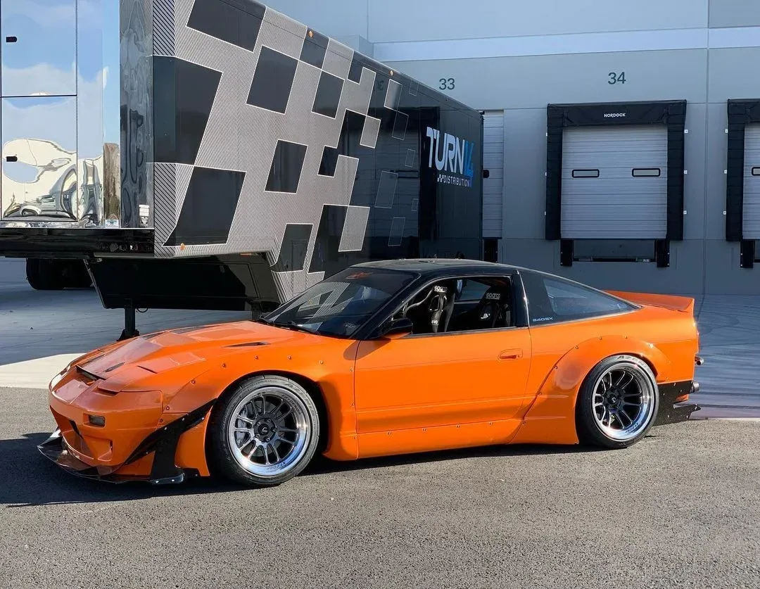 Orange S13 hatchback with a black roof, bolt-on wide arches at the front and rear, a front splitter and canards, parked outside a warehouse